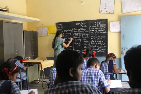 Teacher writing on a blackboard as students learn