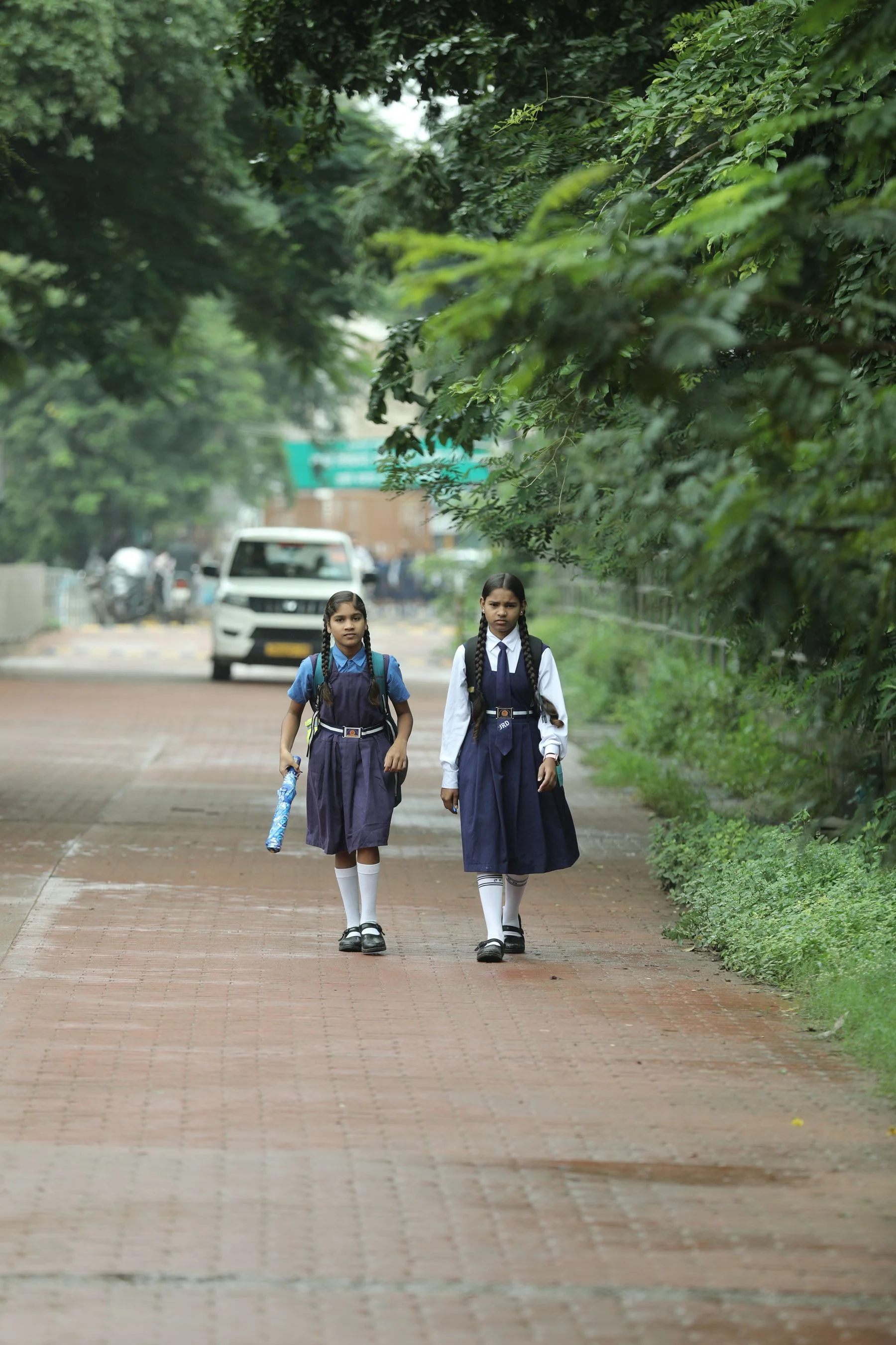 Two students walking along a tree-lined street in Raipur, India