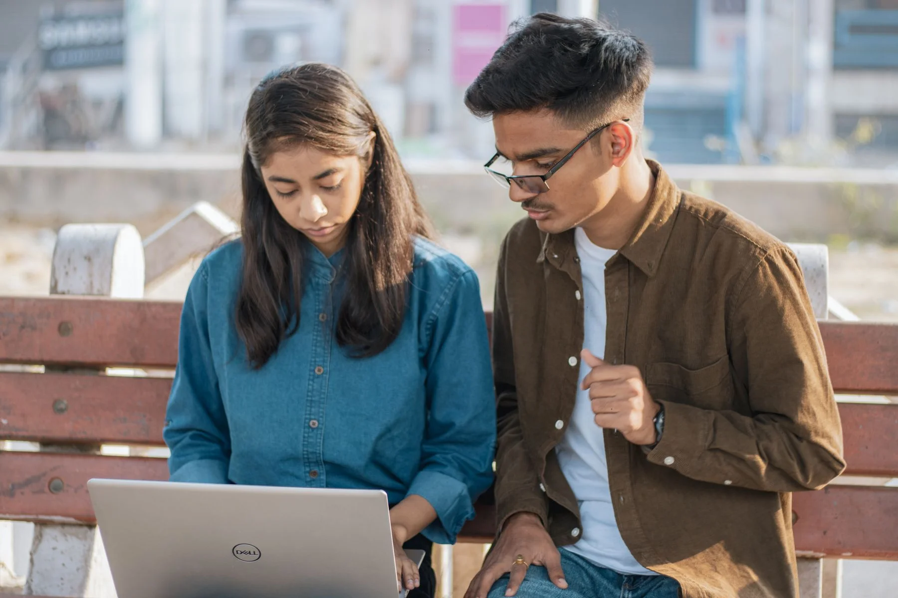 Two young Indian adults studying with a laptop outdoors